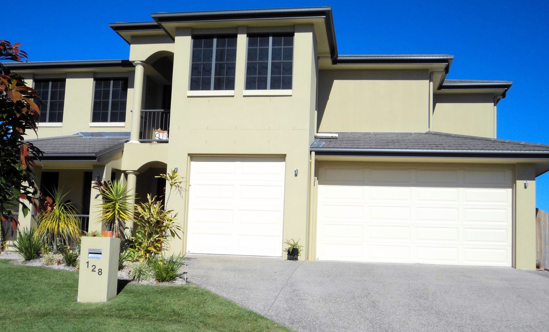 Two-story Beige House With White Garage Doors and a Blue Sky — Coastal Auto Doors & Gates In Palmwoods, QLD