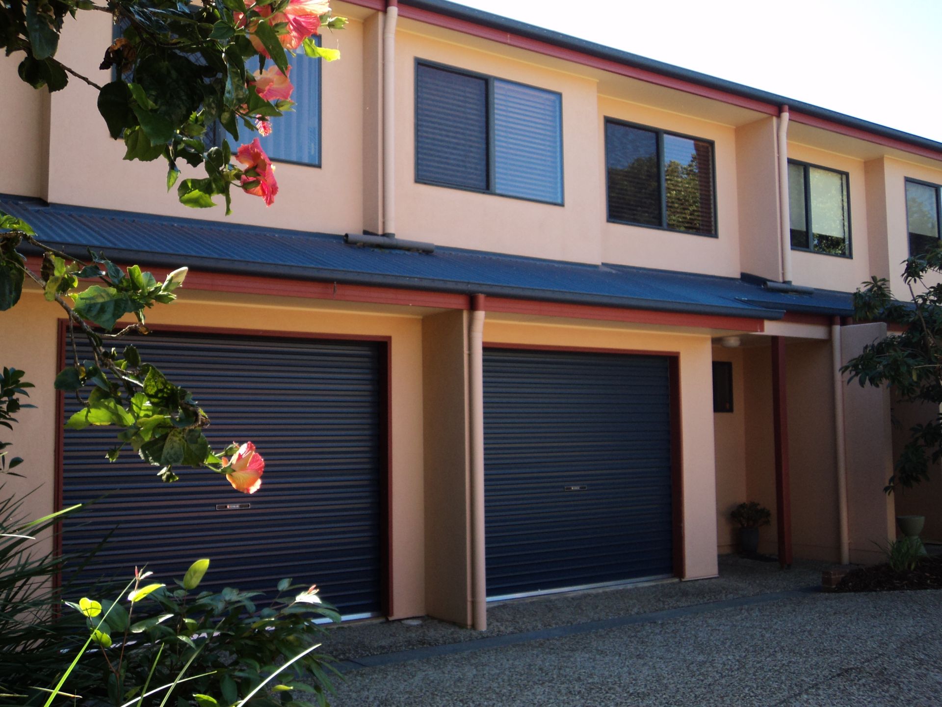 Tan Townhouses With Blue Garage Doors and Windows, Gravel Driveway — Coastal Auto Doors & Gates In Palmwoods, QLD