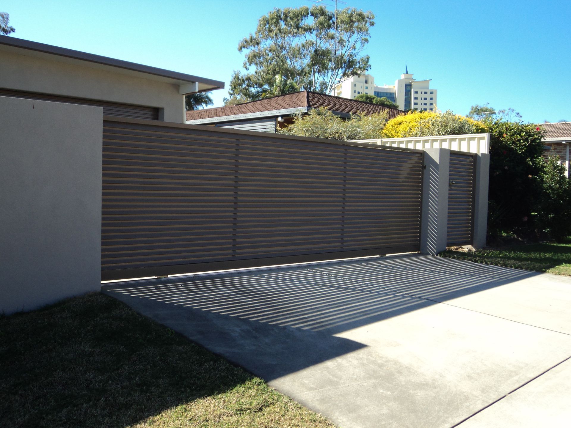 Brown Wooden Gate Across a Concrete Driveway, Casting Shadows — Coastal Auto Doors & Gates In Palmwoods, QLD