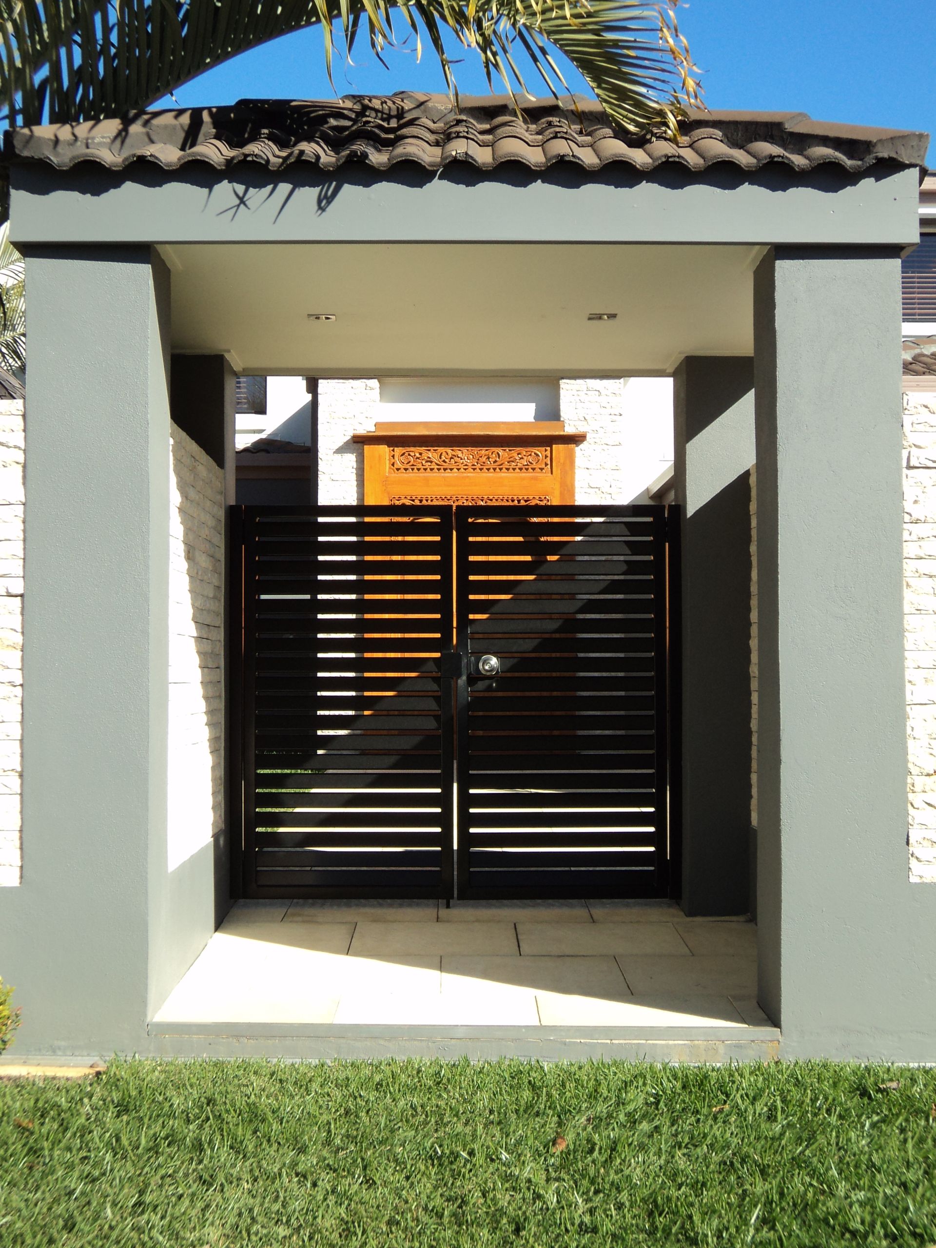 Black Metal Gate Within a Gray-framed Entrance With a Tiled Roof — Coastal Auto Doors & Gates In Palmwoods, QLD