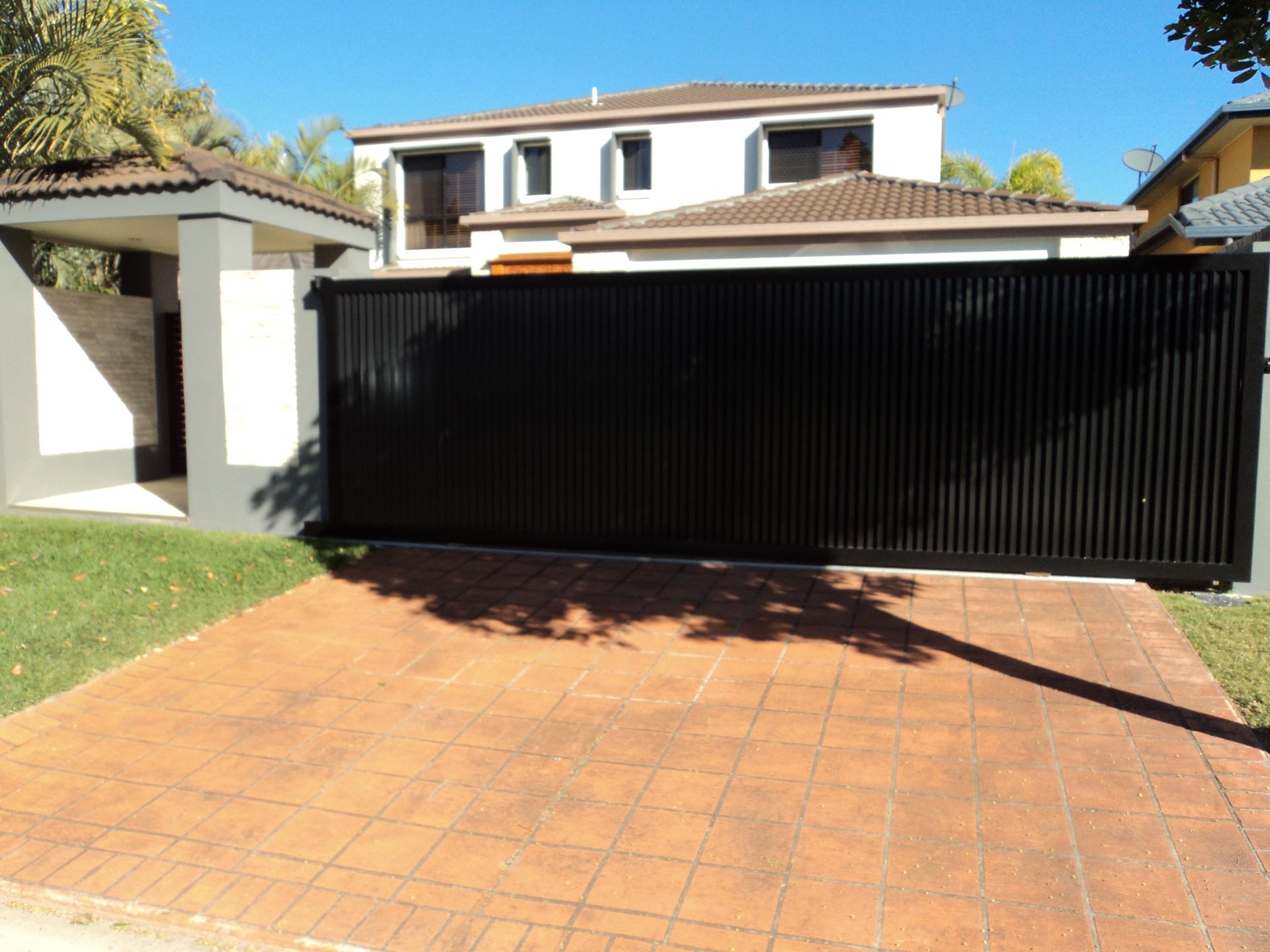 Black Gated Driveway Leading to a White House With Brown Roof — Coastal Auto Doors & Gates In Palmwoods, QLD
