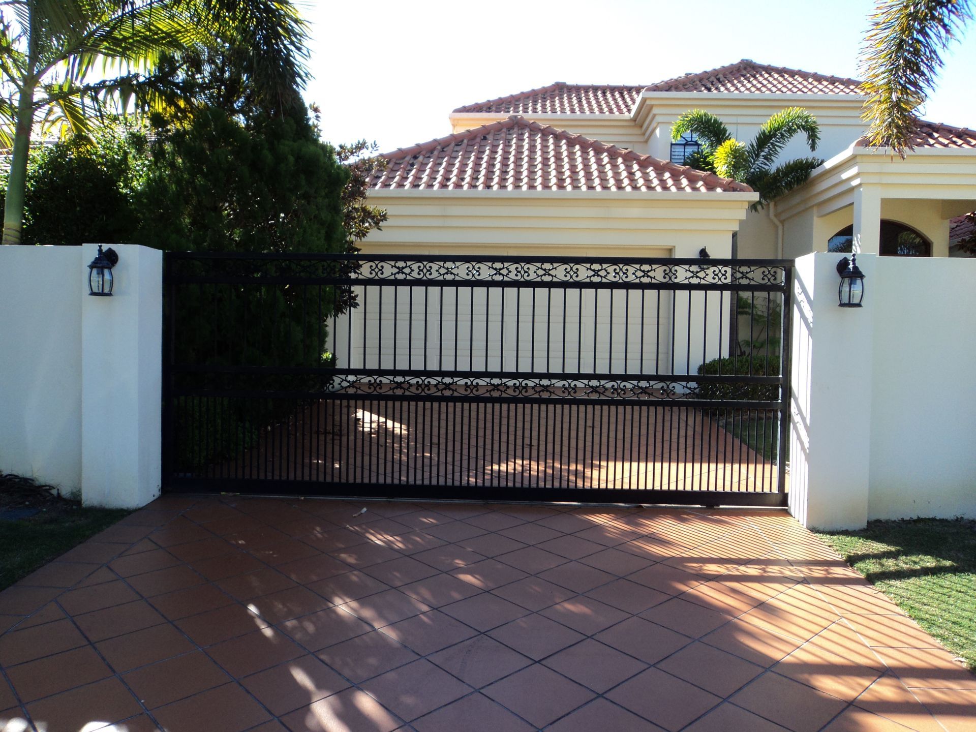 Black Iron Driveway Gate in Front of a Light-colored House — Coastal Auto Doors & Gates In Palmwoods, QLD