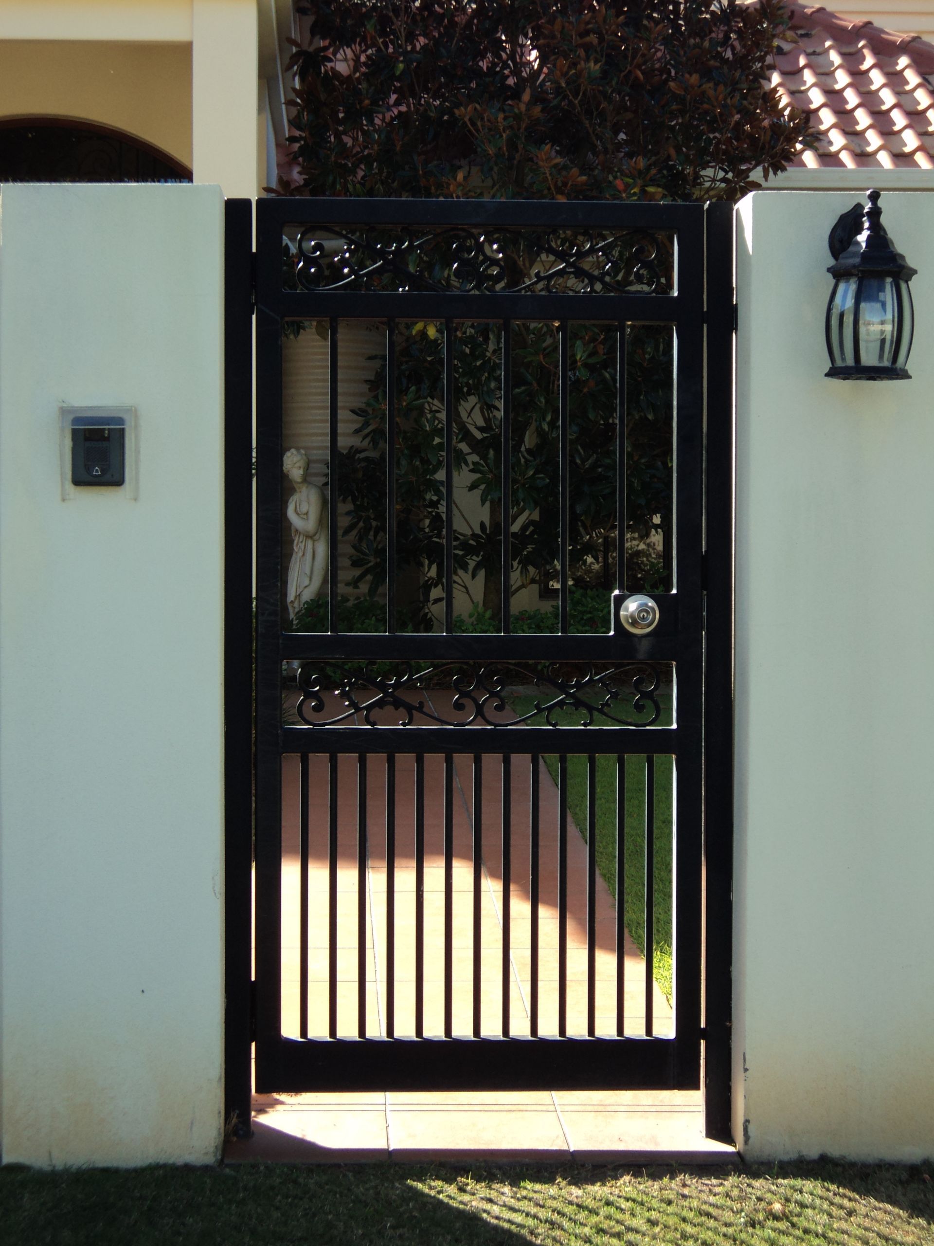 Black Wrought Iron Gate Set in White Walls, Revealing a Glimpse of a Garden — Coastal Auto Doors & Gates In Palmwoods, QLD