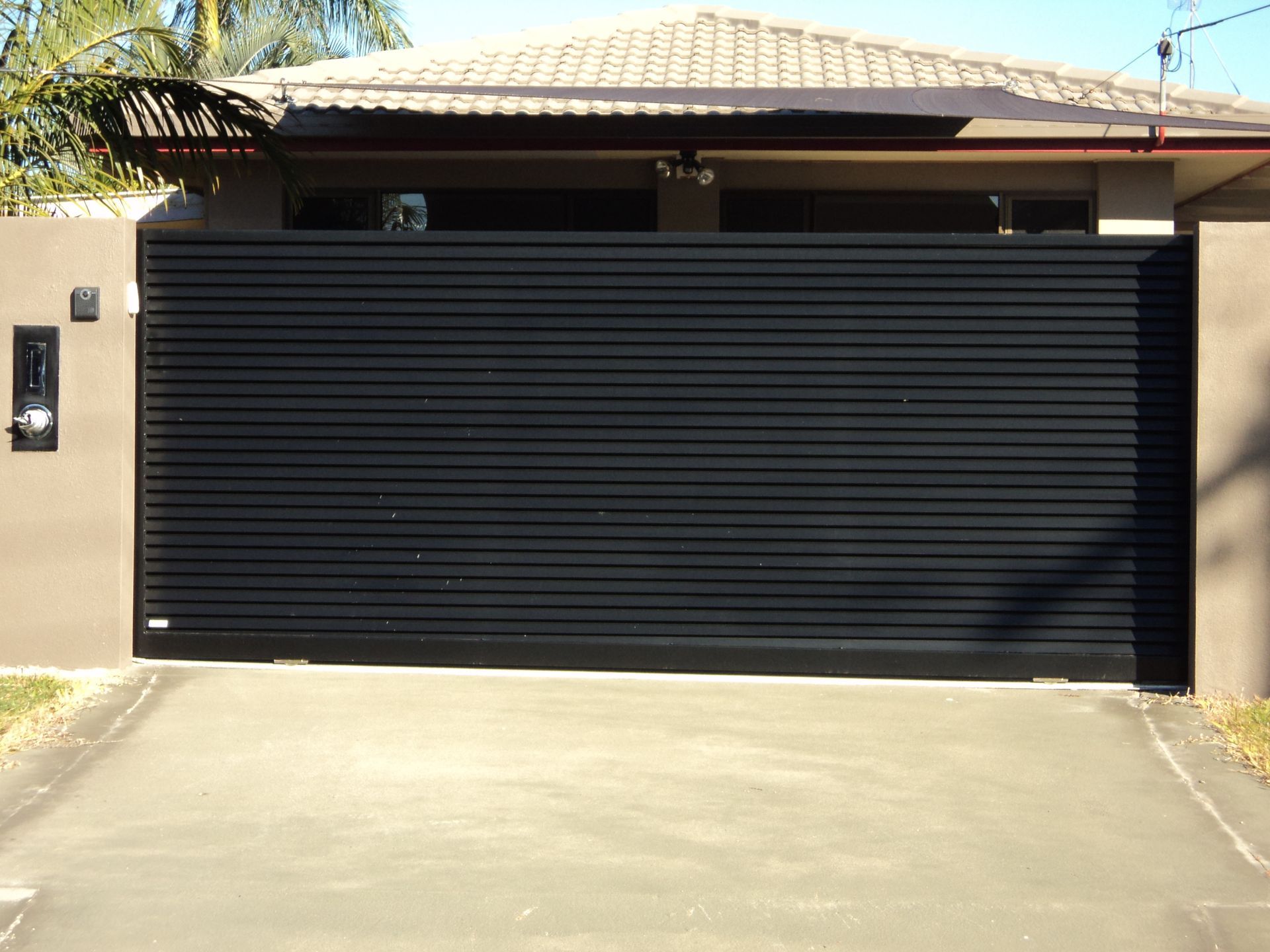 Black Horizontal Slat Driveway Gate. Concrete Driveway, Beige Pillars — Coastal Auto Doors & Gates In Palmwoods, QLD