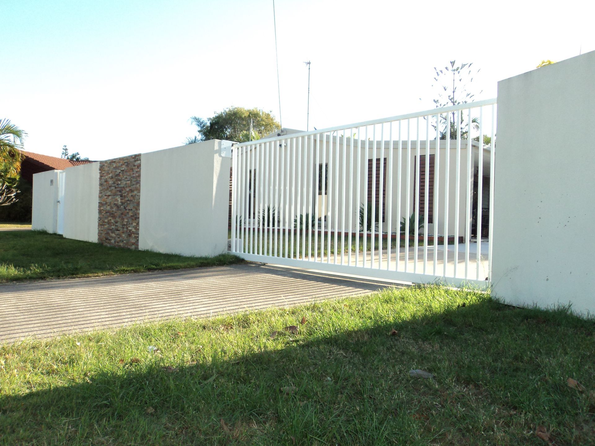 A Driveway With A Sliding Gate In Front Of A House — Coastal Auto Doors & Gates In Maroochydore, QLD