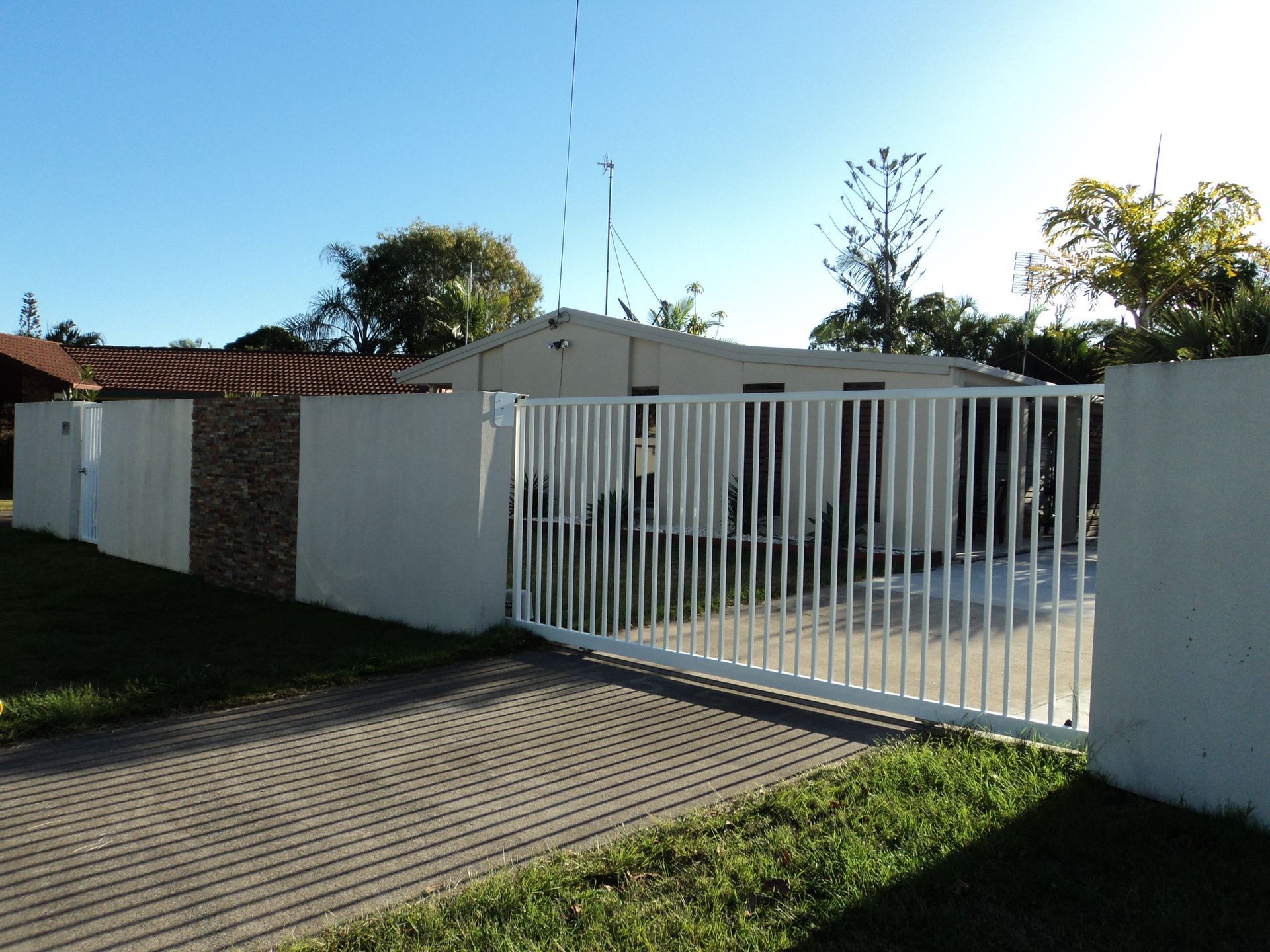 White Gate and Wall Enclosing a House With a Paved Driveway — Coastal Auto Doors & Gates In Sunshine Coast, QLD
