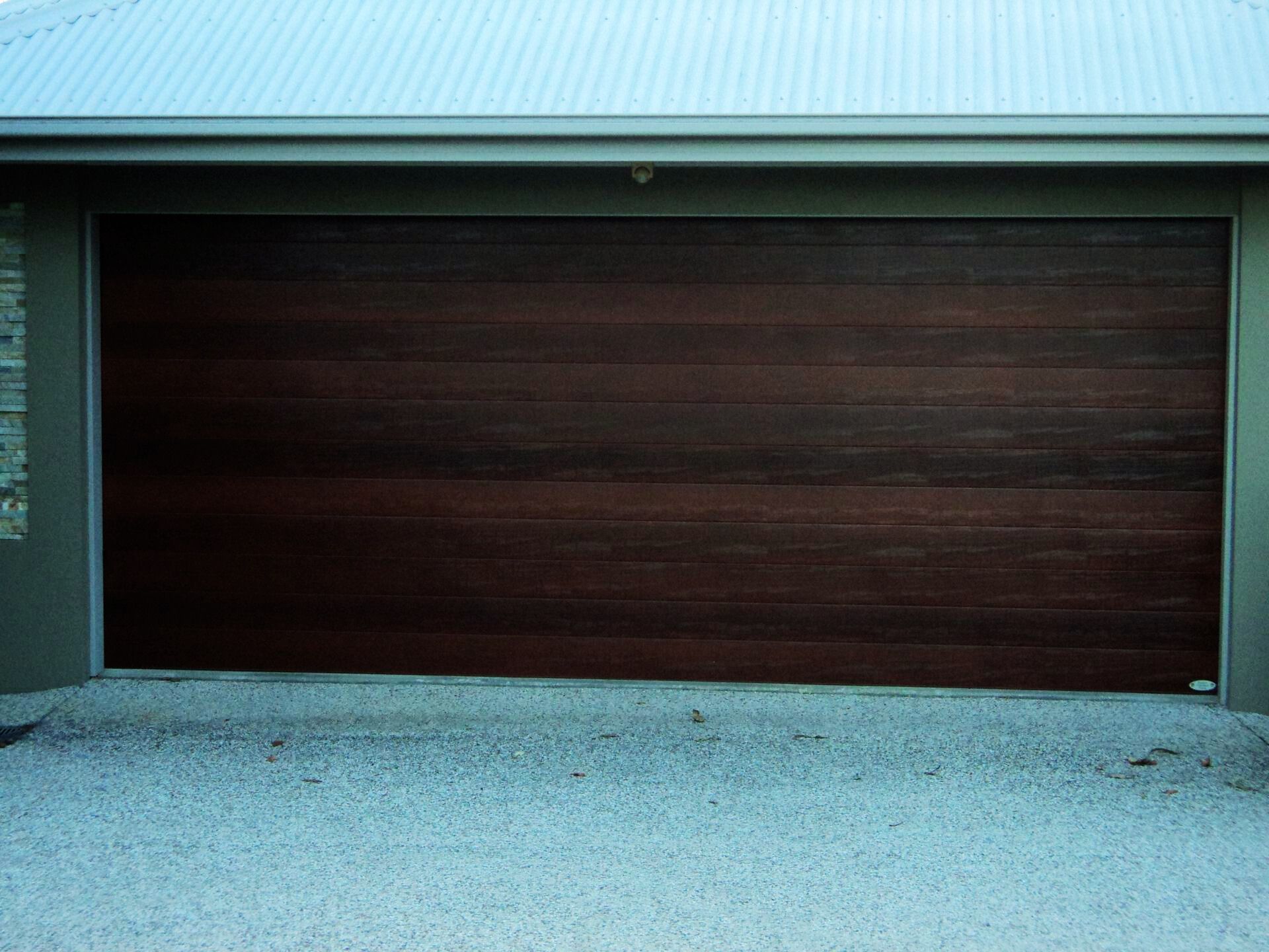 Dark Wooden Garage Door on a Light-colored Gravel Driveway — Coastal Auto Doors & Gates In Caloundra, QLD