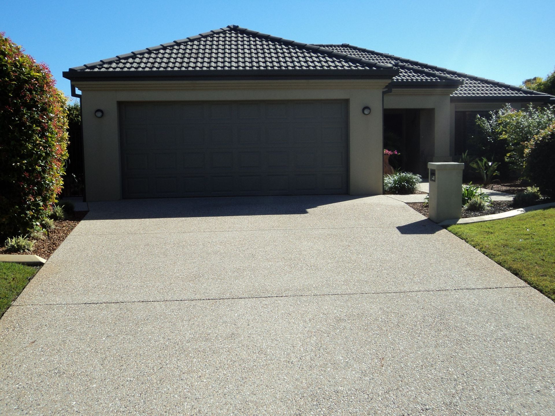 Beige House With a Concrete Driveway and Gray Garage Door, Sunny Day — Coastal Auto Doors & Gates In Palmwoods, QLD