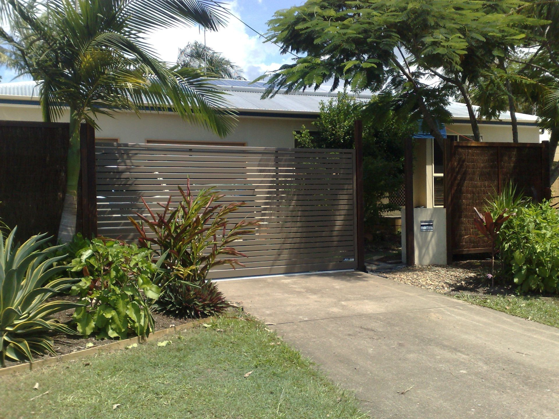 Wooden Gate at Driveway Entrance With Surrounding Greenery and House — Coastal Auto Doors & Gates In Buderim, QLD