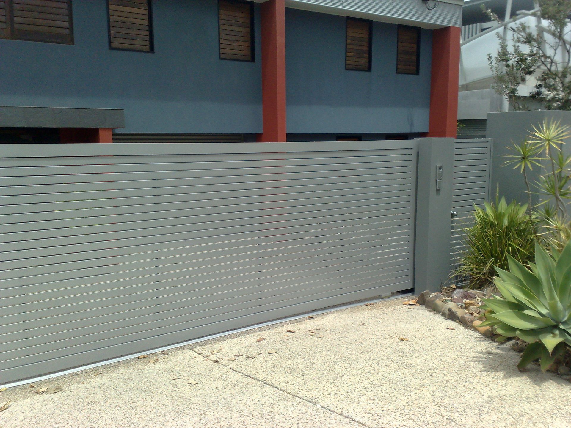 Gray, Perforated Metal Sliding Gate in Front of a Blue Building — Coastal Auto Doors & Gates In Sunshine Coast, QLD