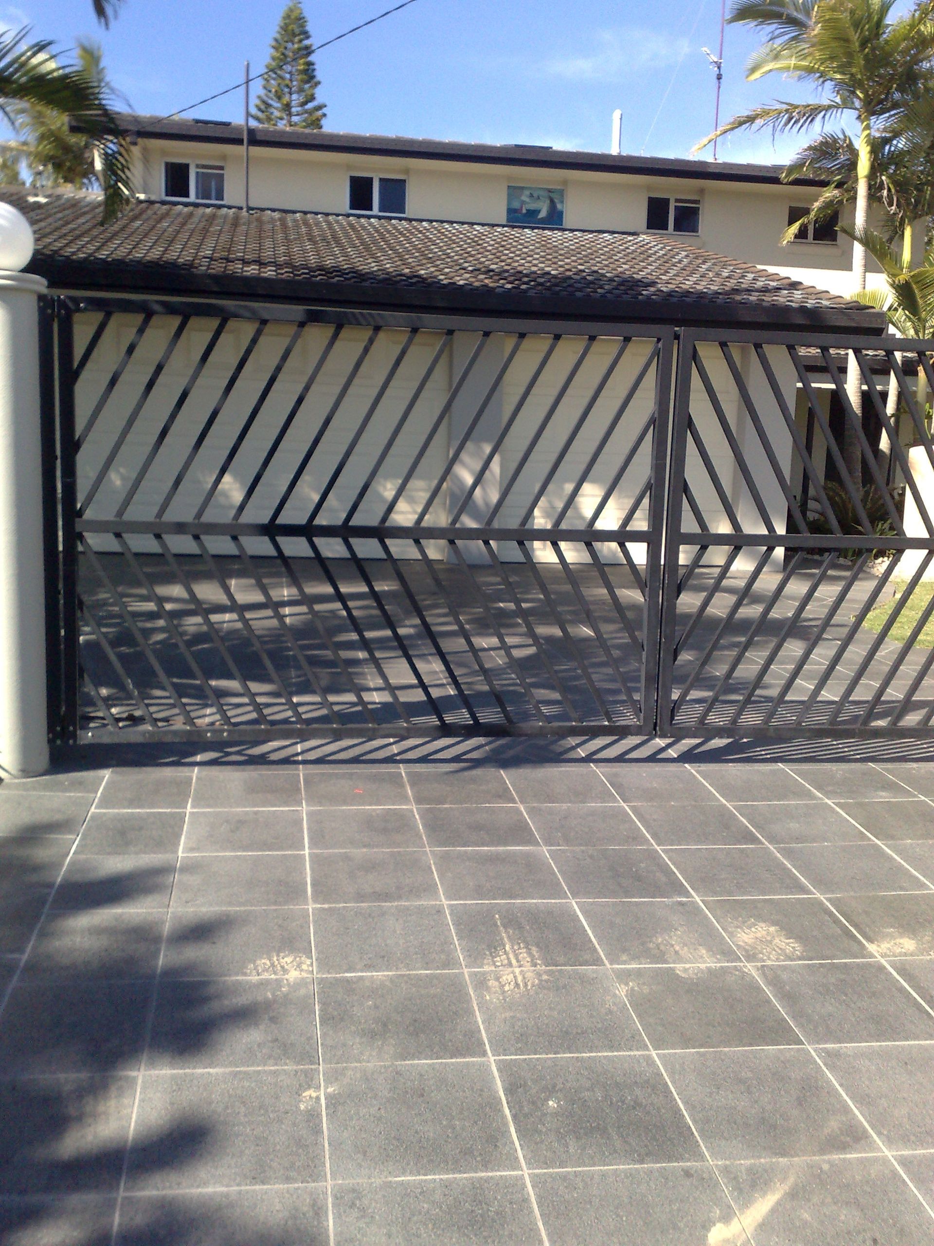 Black Gate With Diagonal Bars in Front of a Light-colored Building — Coastal Auto Doors & Gates In Palmwoods, QLD