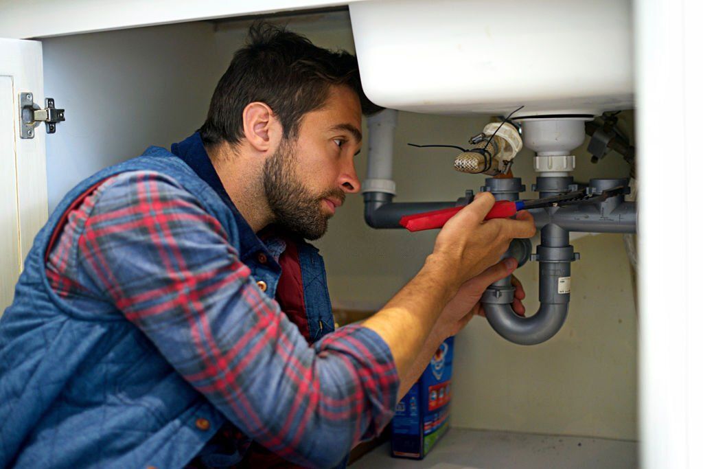 A man is fixing a sink pipe with a wrench.