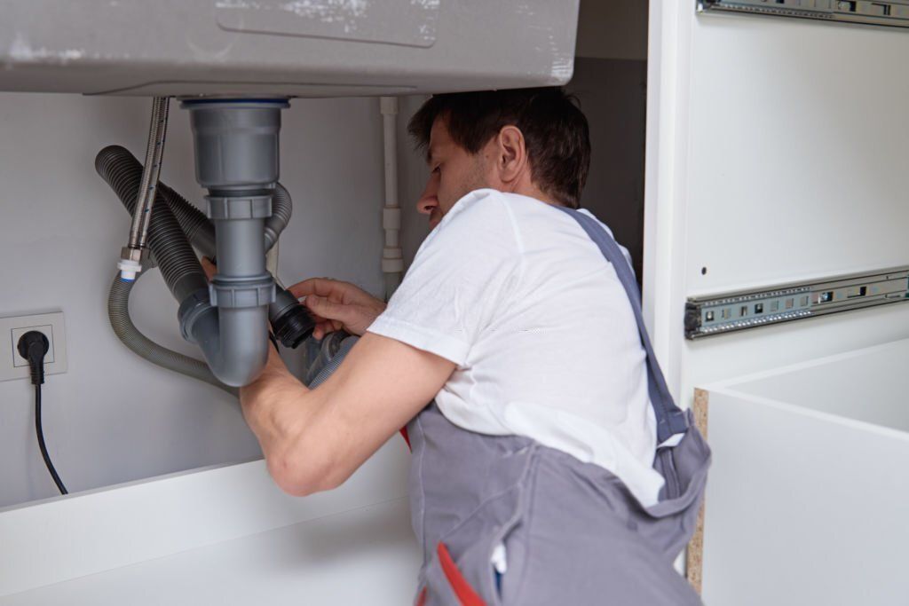 A man is fixing a sink pipe in a kitchen.