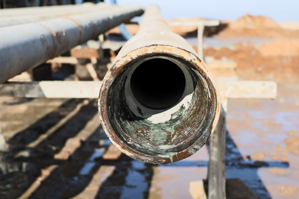 A close-up view of an open-ended metal pipe at an industrial site with a light-colored, residue-lined interior.