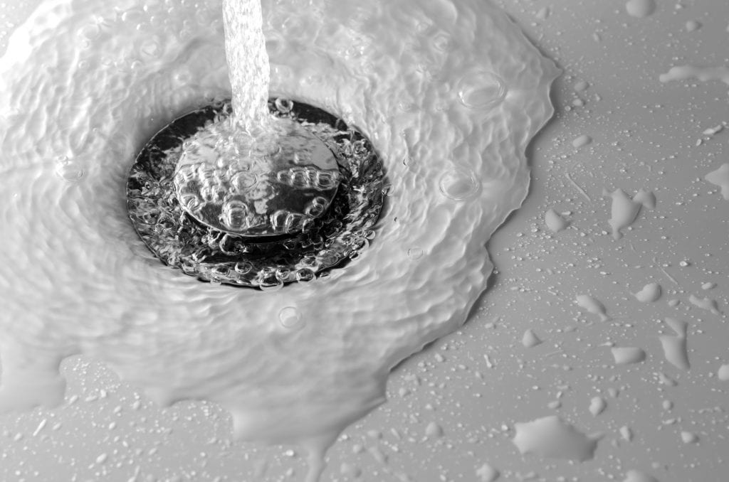 A black and white photo of drain water draining slowly water running down a sink drain.