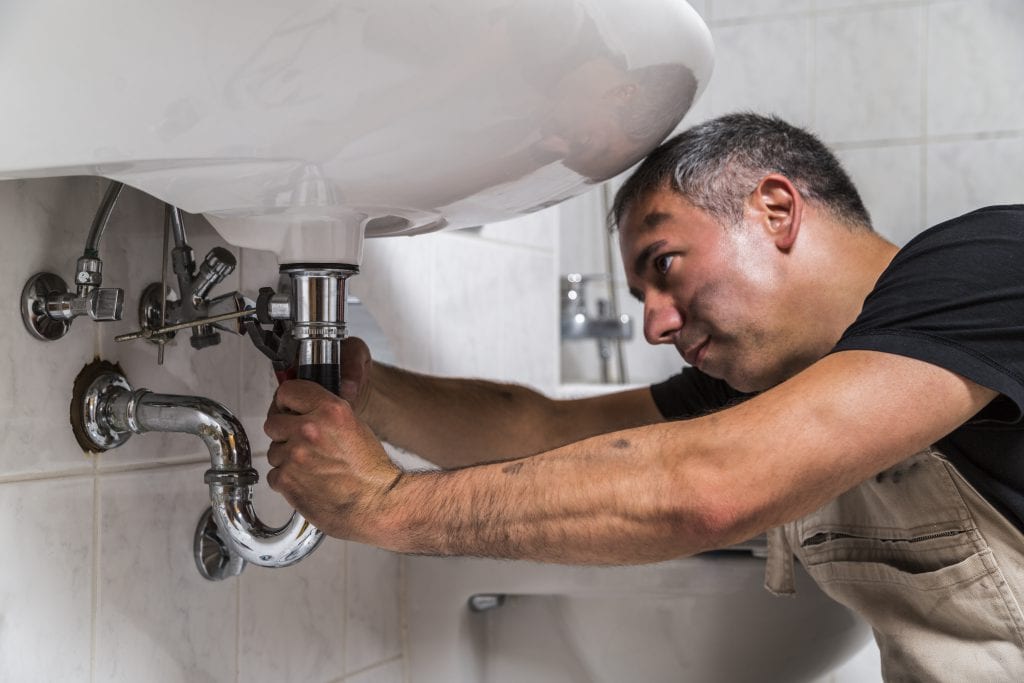 A plumber is fixing a sink in a bathroom.