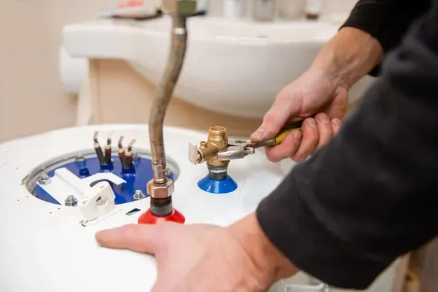 Hands using an adjustable wrench to tighten a brass valve fitting on top of a residential water heater.