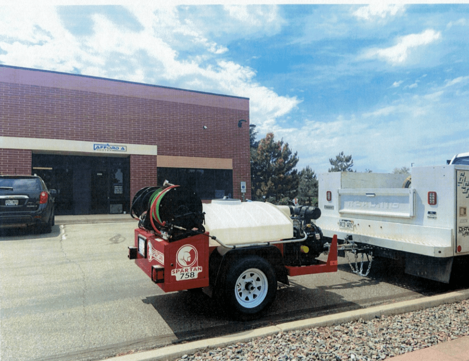 A trailer with a hose attached to it is parked in front of a building