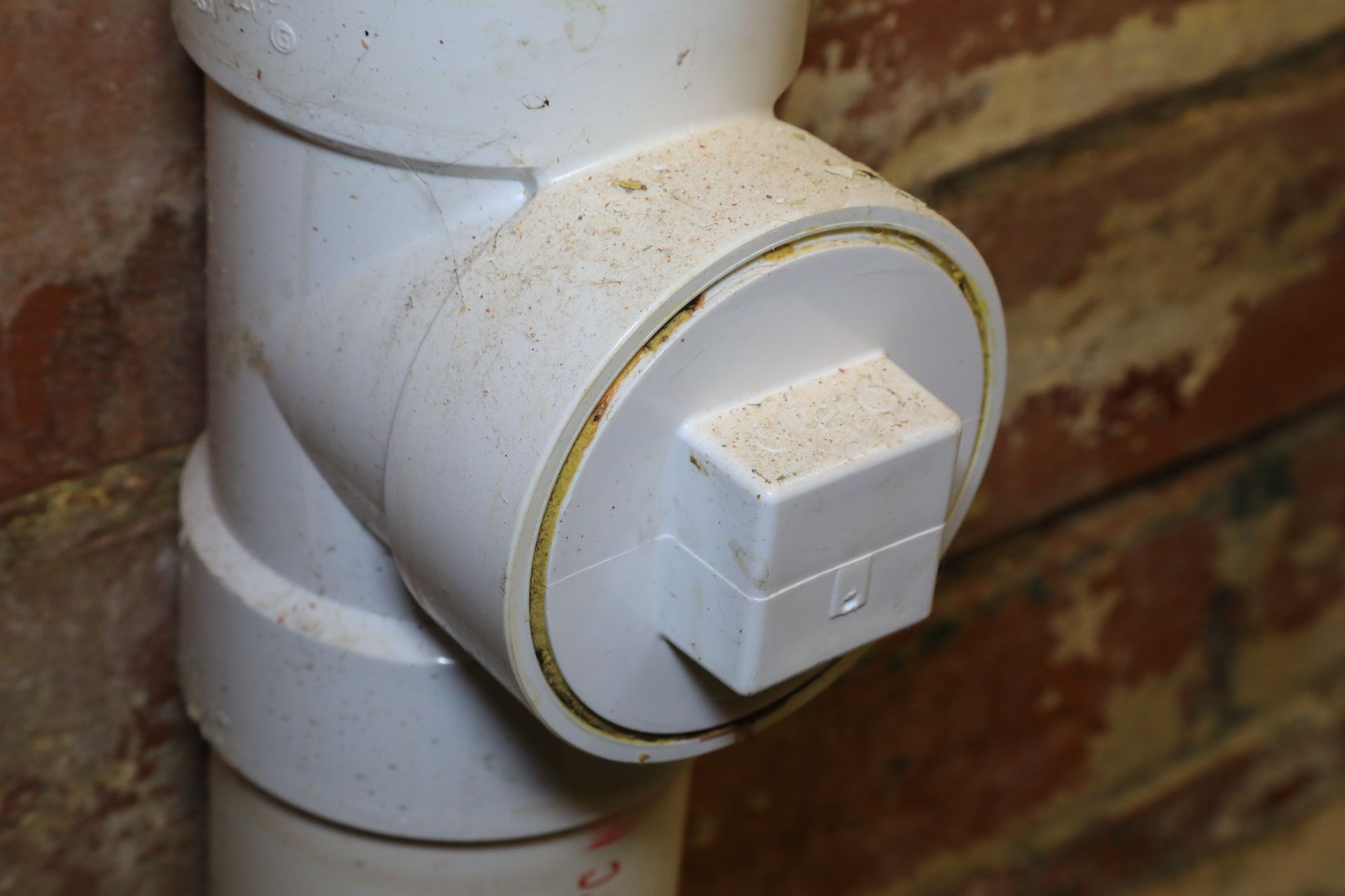 A close up of a white pipe against a brick wall.