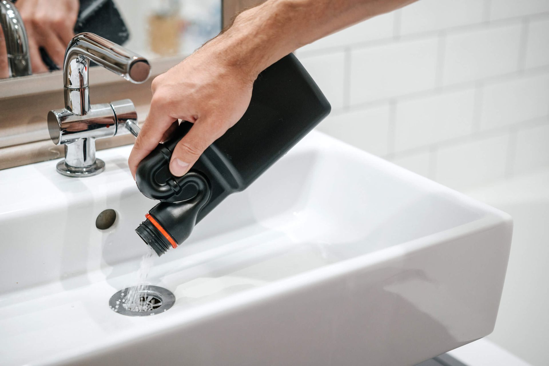 A person is pouring a bottle of drain cleaner into a bathroom sink.