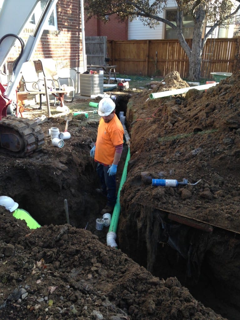 A man in an orange shirt is digging a hole in the dirt.