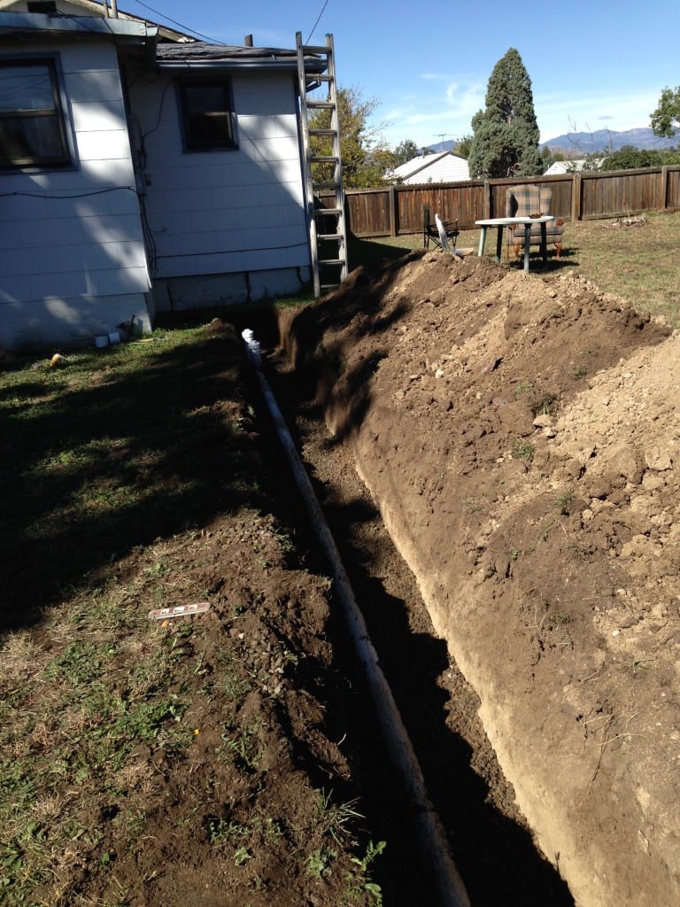 A pipe is being installed in a backyard next to a house.