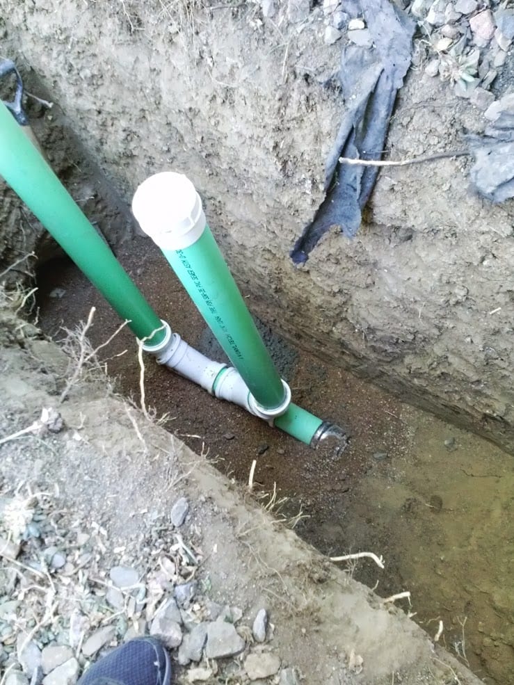 Two green pipes are in a hole in the ground.