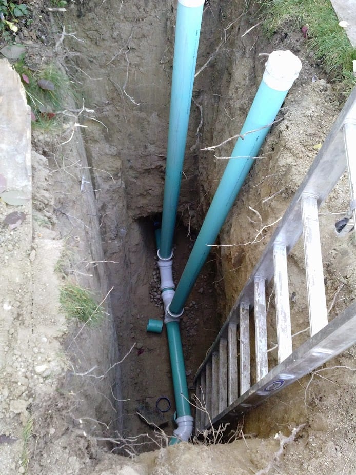 A ladder is going down a hole with green pipes