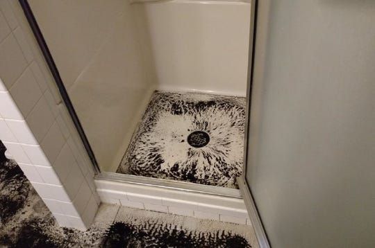 A shower stall with a dirty floor and a black rug.