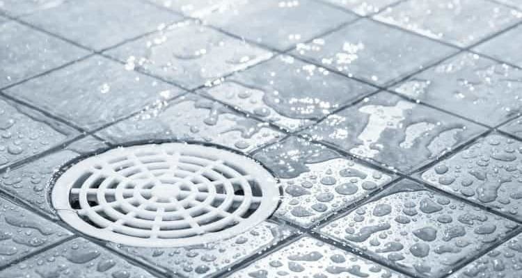 A drain on a tiled floor with water drops on it.