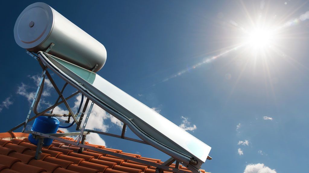 A solar water heater is sitting on top of a tiled roof.