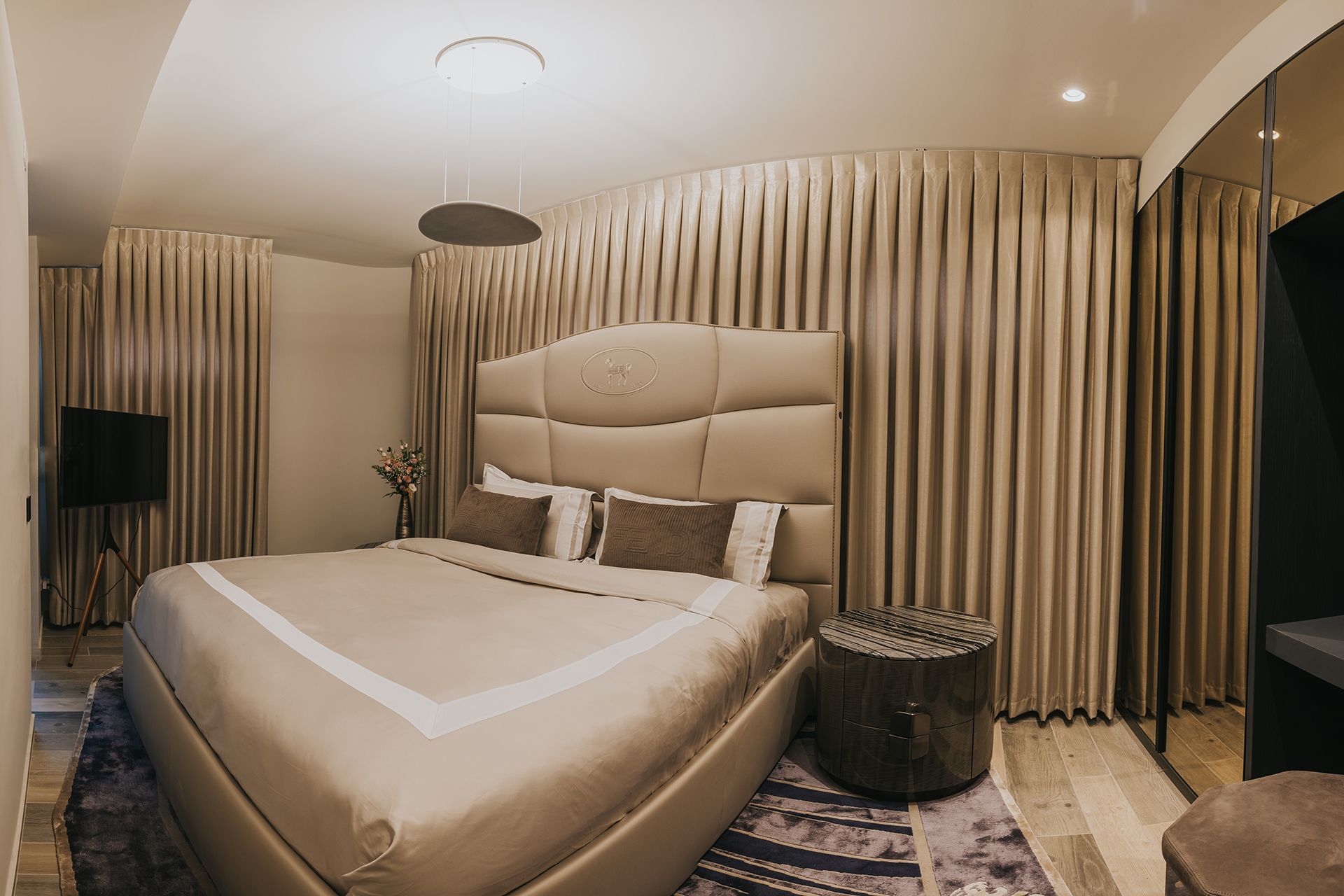 Bedroom with a large bed, beige curtains, and wooden bedside table.