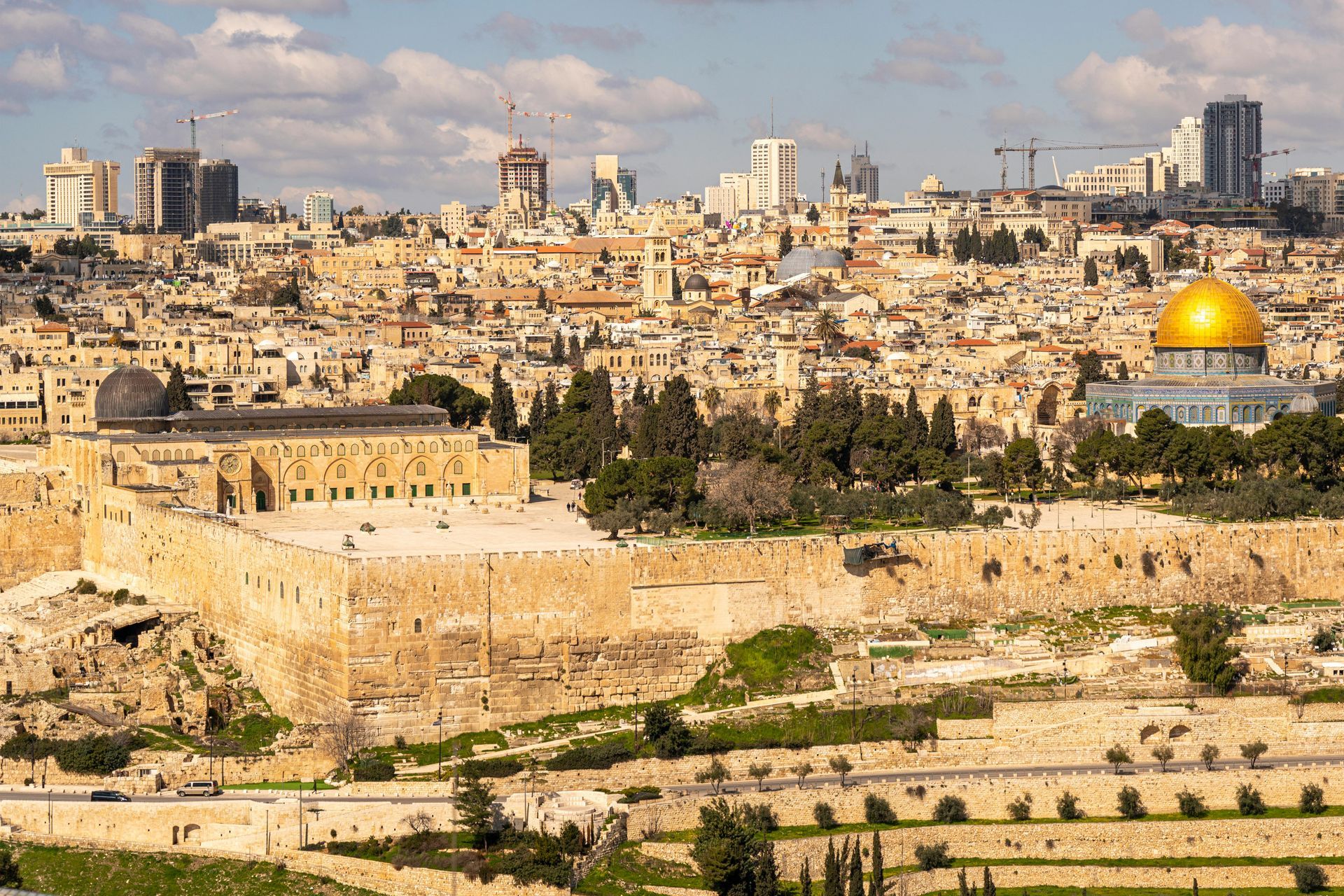 Jerusalem cityscape with the Dome of the Rock and Al-Aqsa Mosque; golden dome, tan buildings, blue sky.