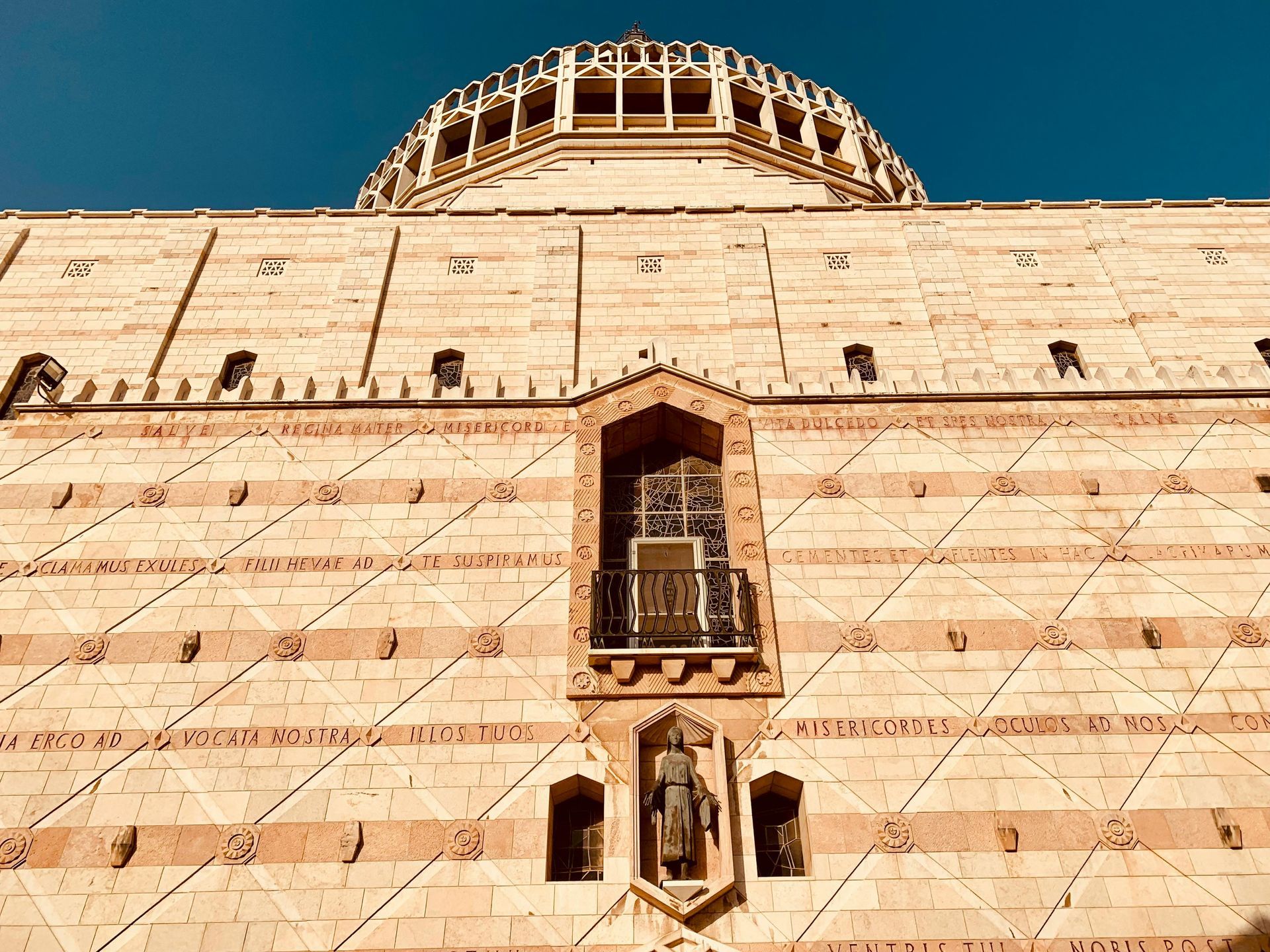 Exterior of the Basilica of the Annunciation in Nazareth, Israel, with stone facade and domed roof against a blue sky.