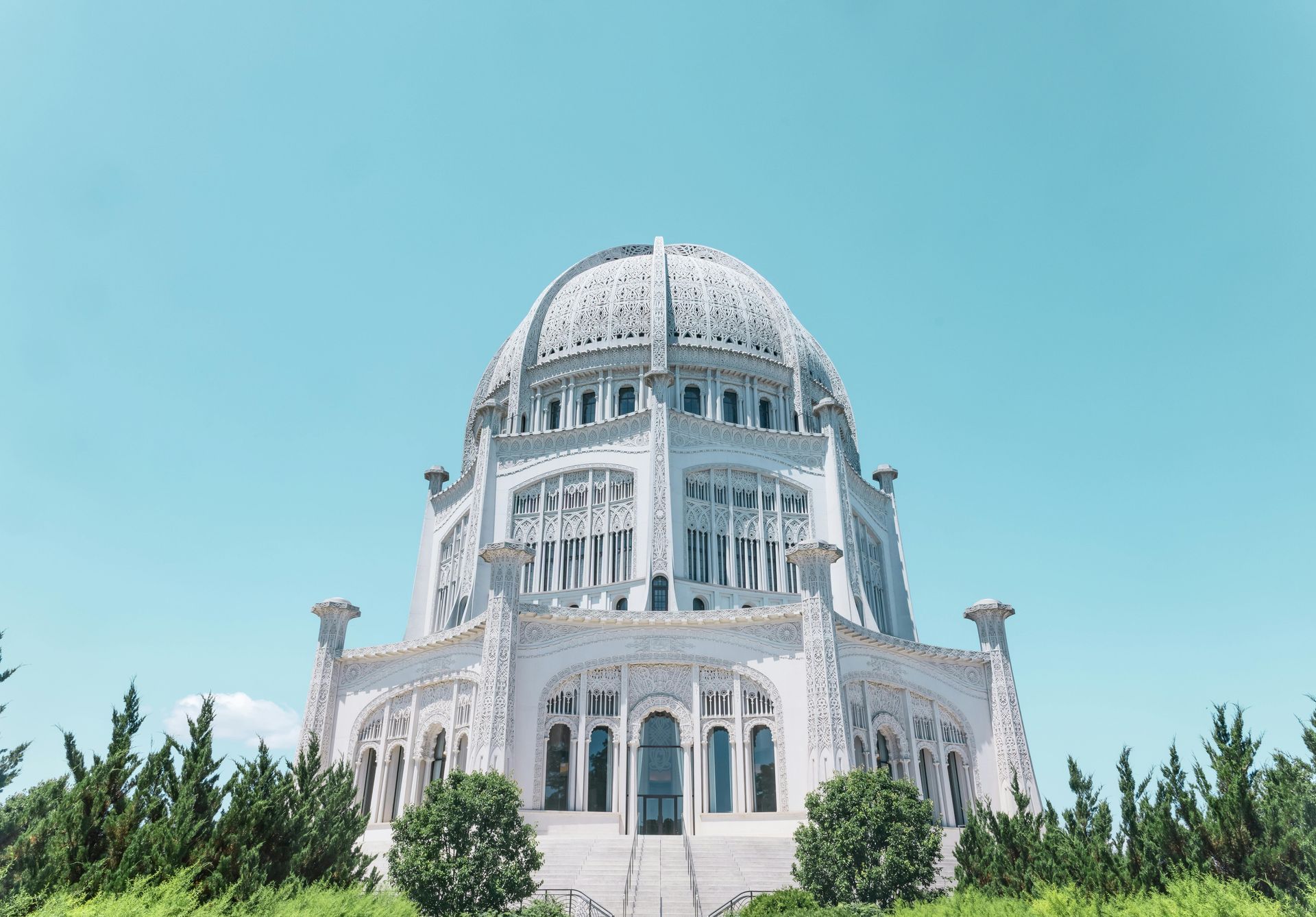 White Baháʼí House of Worship in Wilmette, Illinois, with intricate dome and blue sky backdrop.