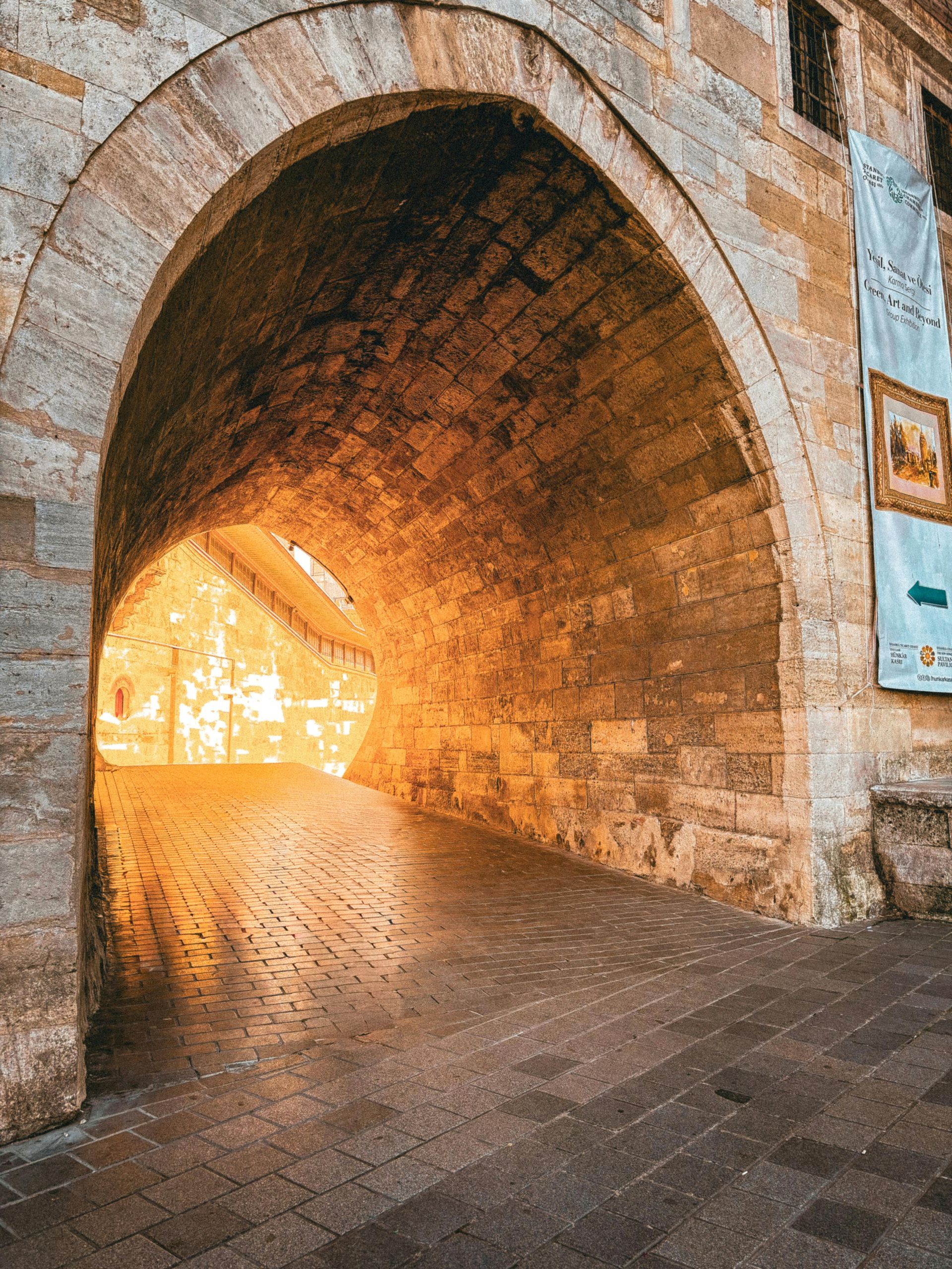 Stone archway leading to a bright, sunlit space; textured brick, cobblestone floor.