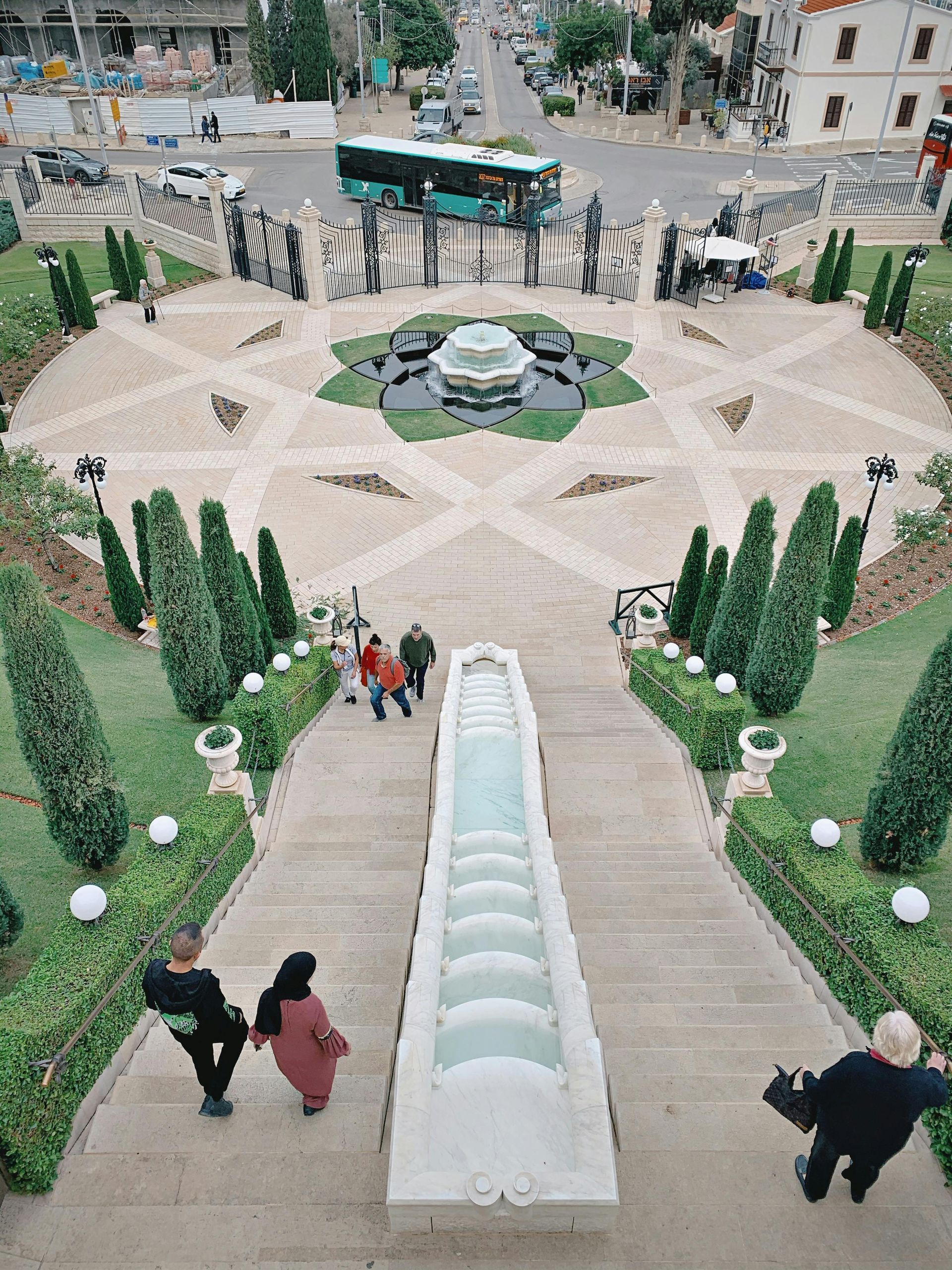 Stone steps leading up to gardens with a fountain, cars, and a bus in the background. People walking.