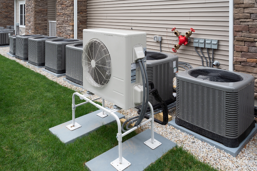 A row of air conditioners are sitting outside of a house.