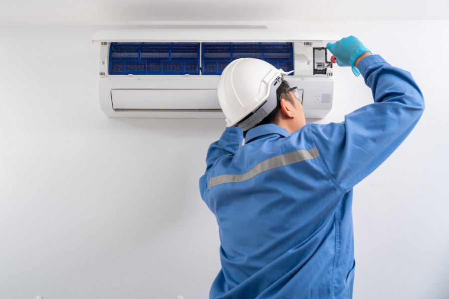 A man wearing a hard hat and gloves is working on an air conditioner.