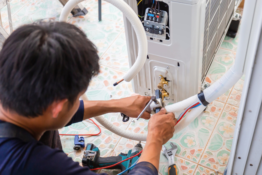 A man is fixing an air conditioner with a wrench.