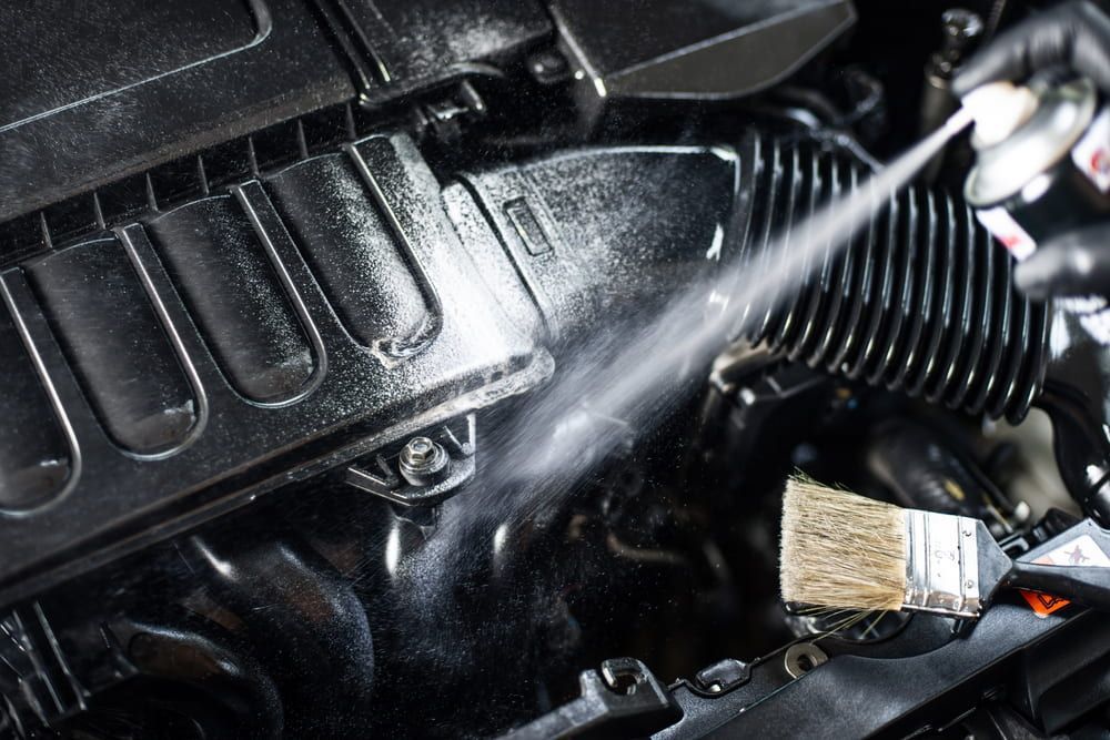 Person Spraying Cleaning Solution on a Black Car Engine With a Brush Nearby — Burcher EFI & Service Centre in Orange, NSW
