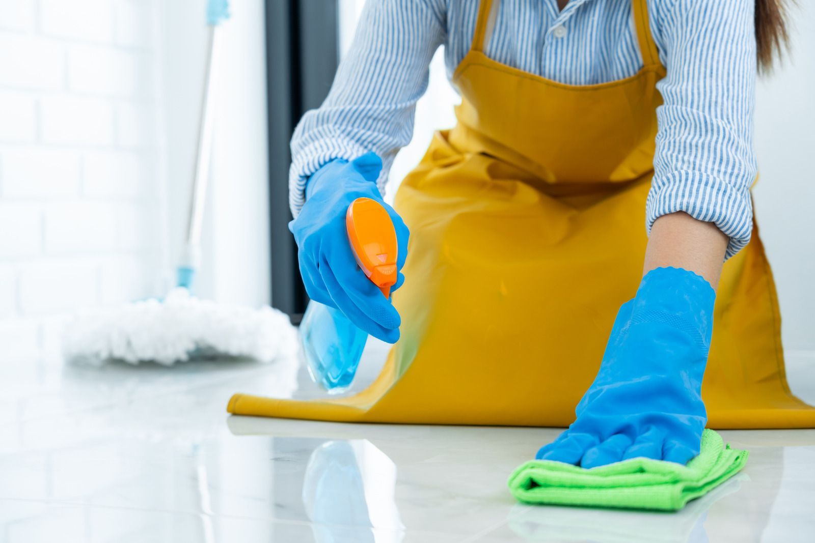 A woman in a yellow apron and blue gloves is cleaning the floor.