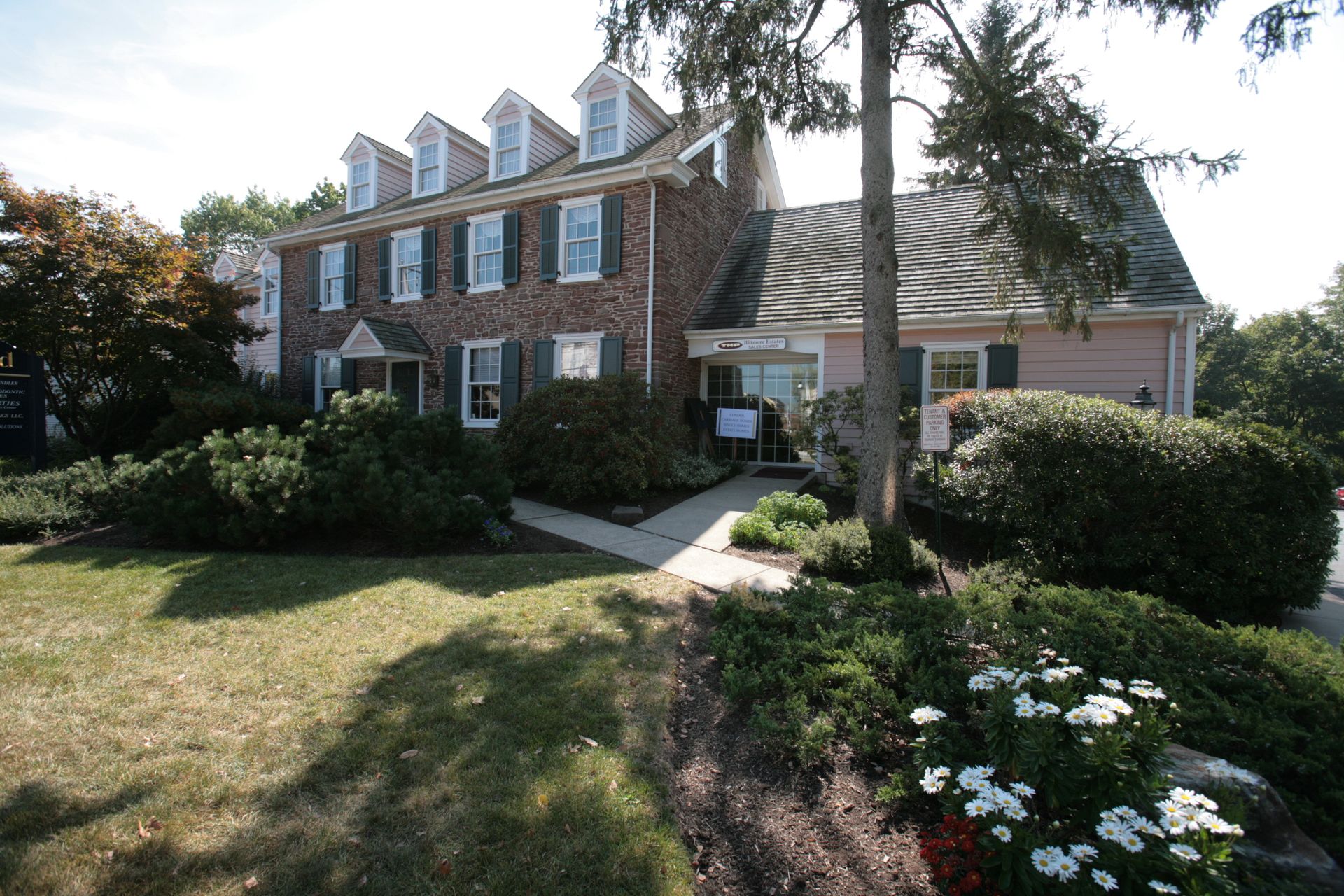 Brick building with white trim, green shutters, and landscaping, featuring a lawn and flower beds.