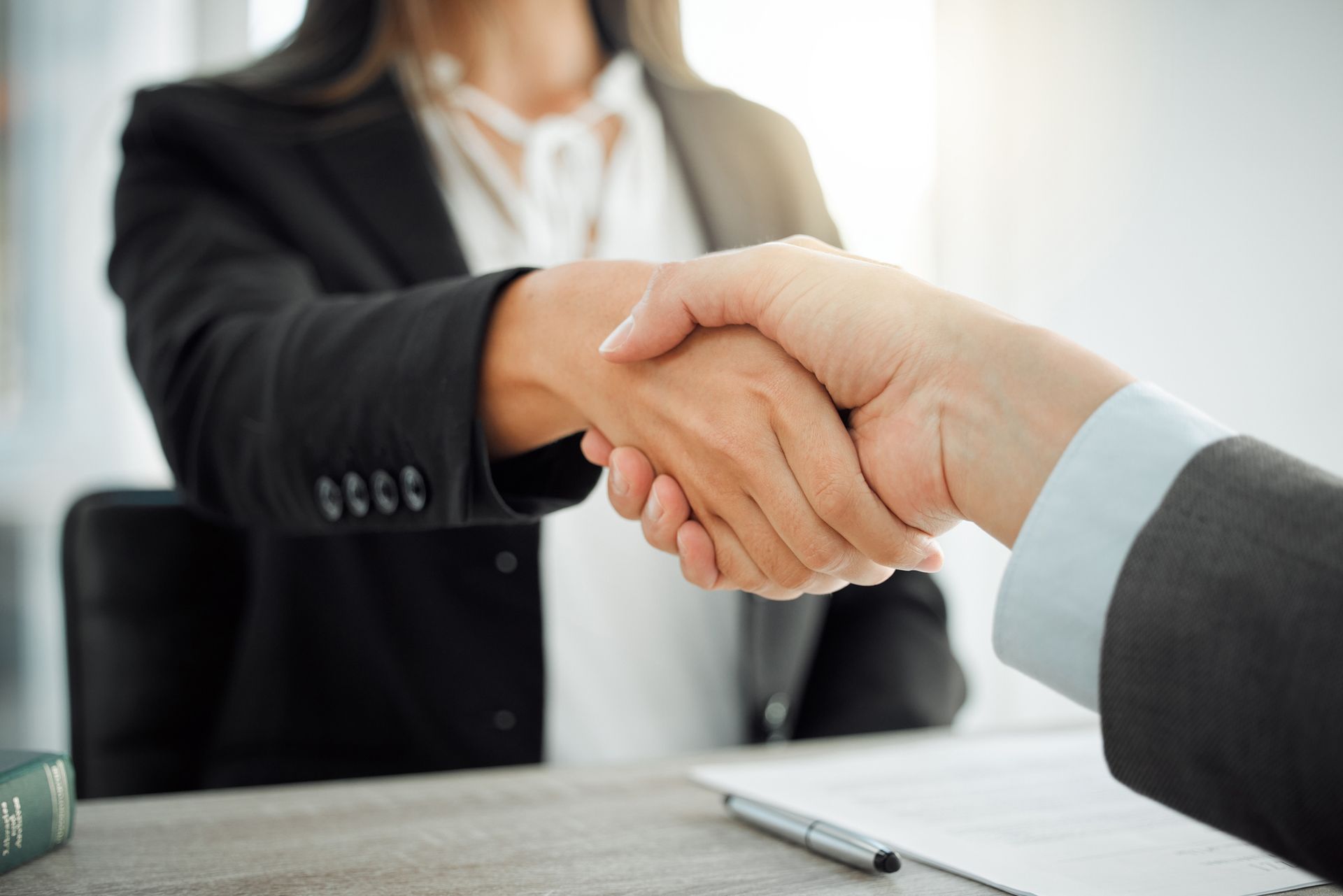 Two people in business suits shaking hands at a desk.
