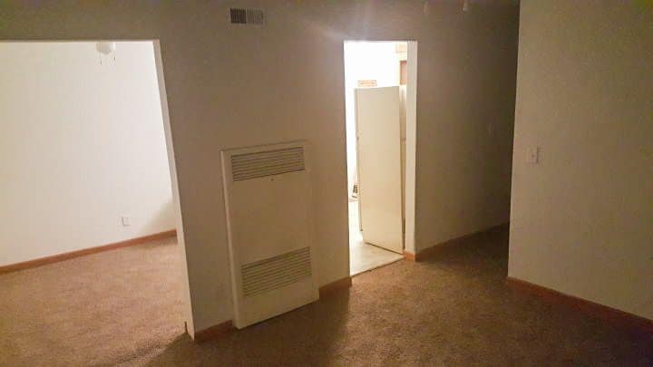 An empty room with a doorway leading to a bathroom and a refrigerator.
