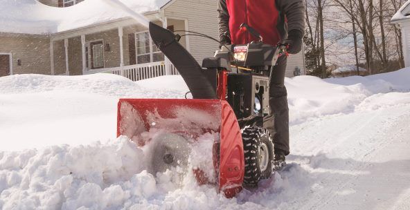 A man is using a snow blower to clear snow from a driveway.