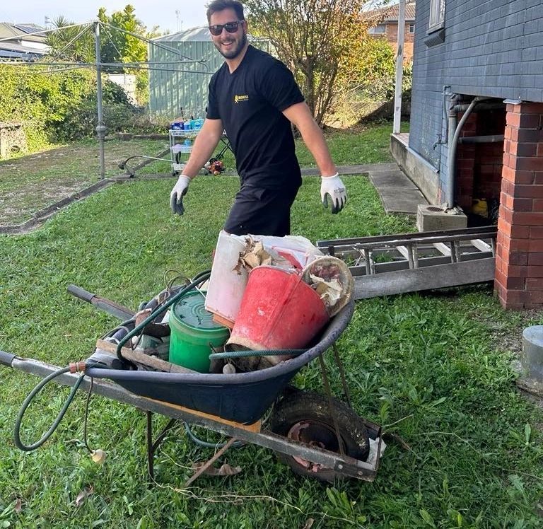 A man is pushing a wheelbarrow full of buckets and a ladder