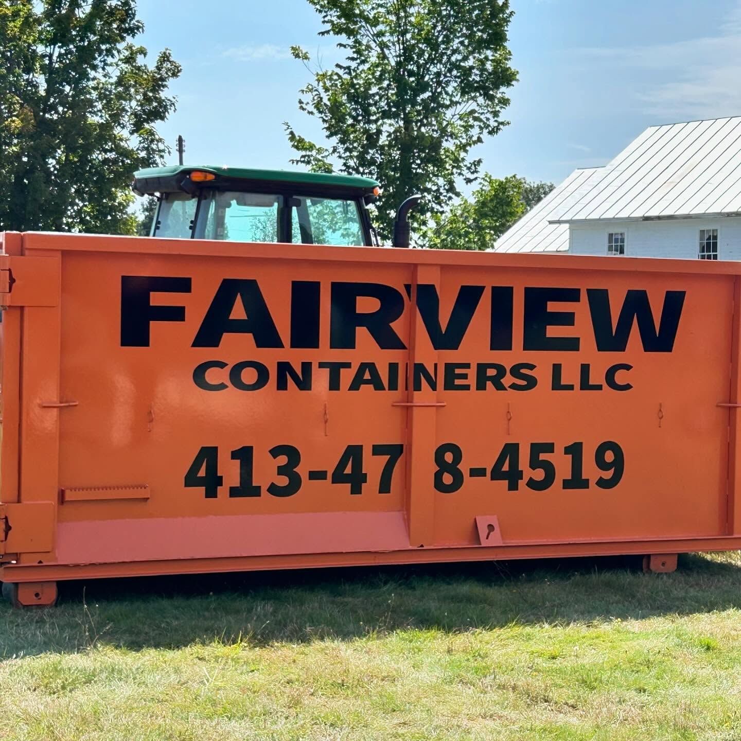 Orange Fairview Containers LLC dumpster, green tractor, and white building in a grassy area.