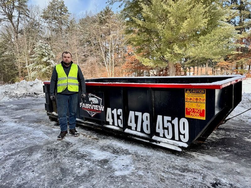 Person in a reflective vest stands beside a black dumpster with the phone number 413-478-4519 in a snowy outdoor setting.