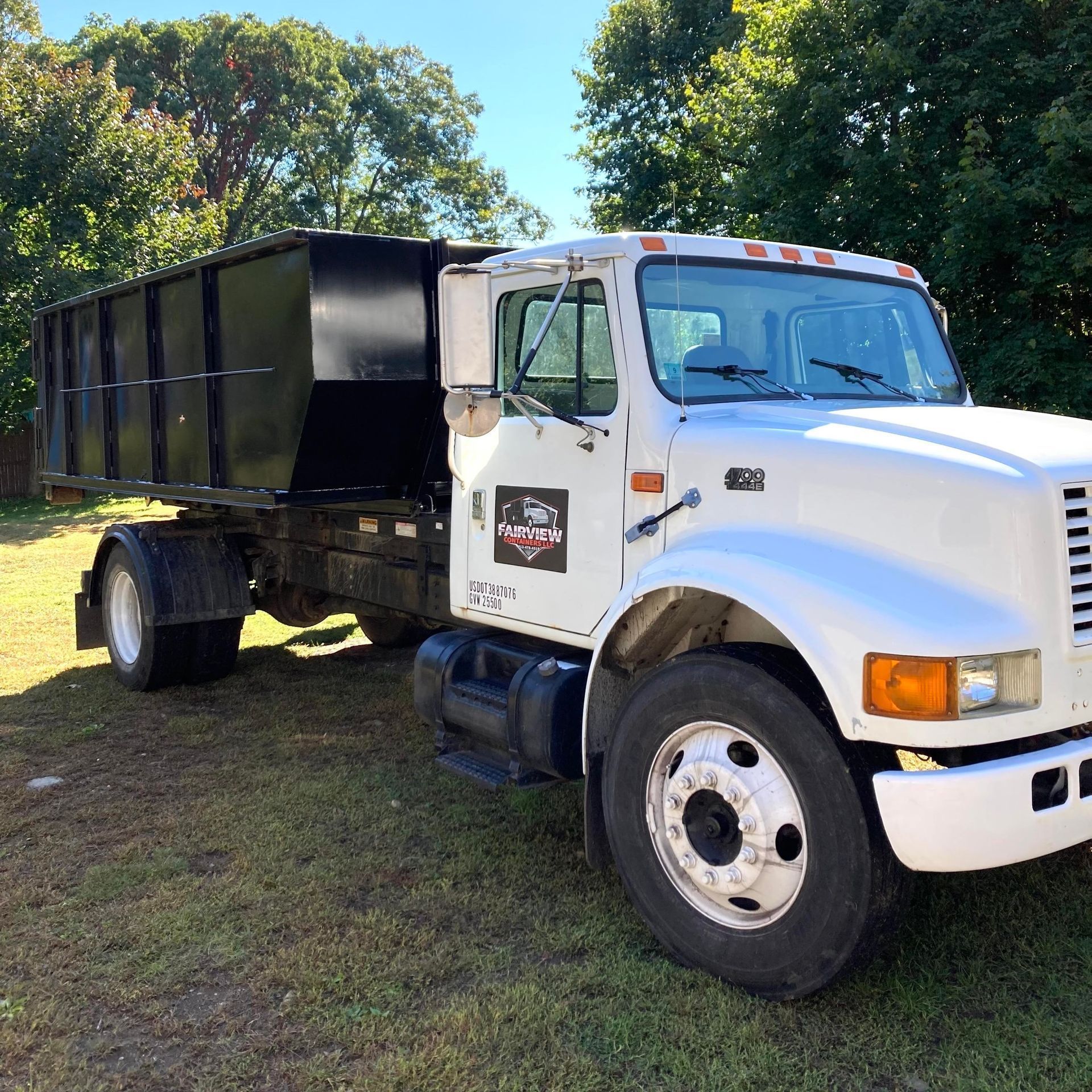 White International truck with a black dumpster bed parked on grass.